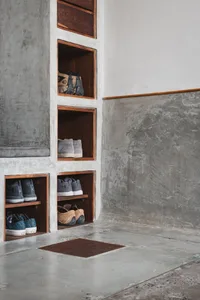 Concrete wall with built-in shelves storing various shoes and bags in a minimalist industrial design.