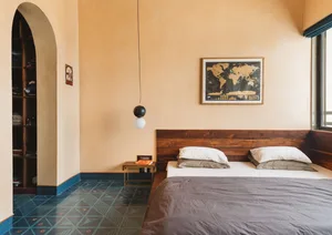 A minimalist bedroom featuring wooden furniture, a concrete floor with geometric patterns, and a world map on the wall.