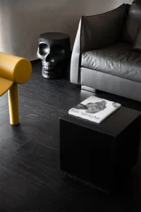 A minimalist interior space featuring a black leather armchair, a wooden coffee table, and a decorative skull stool.