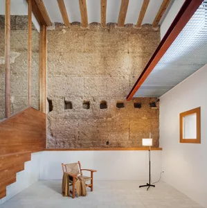 minimalist-style living room with exposed concrete walls and simple wooden furniture, including a chair with a woven backrest