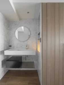 A minimalist modern bathroom with marble walls, a floating sink, and wooden accents.