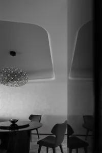 A modern dining room with black and white decor, featuring a round table, chairs, and a geometric chandelier.