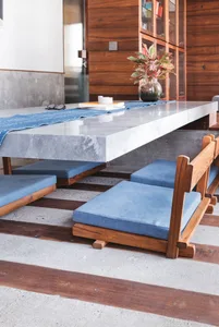 A modern dining room with a concrete table, blue cushions, and a wooden floor.
