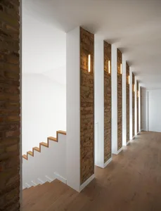 Modern interior design featuring wooden stairs, brick columns, and plaster walls.