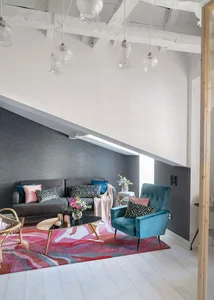 A modern living room featuring a colorful abstract rug, a grey sofa with patterned cushions, a teal armchair, and a black cof