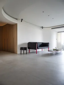 A modern living room featuring a black knitted sofa with red legs and a concrete floor.