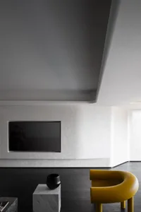 Modern living room featuring minimalist furniture, black and yellow chairs, a marble coffee table, and a flat-screen TV mount