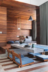 Modern living room designed with wooden walls, a concrete table, and blue seating.