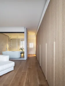 A modern minimalist bathroom with a white bathtub and wooden flooring and walls.