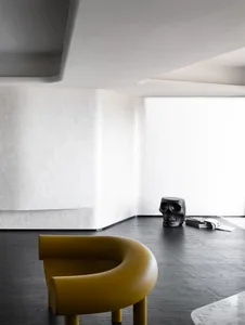 A minimalist interior with a bold mustard yellow rounded chair and a black skull sculpture on a black wooden floor, surrounde