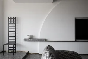 A modern, minimalist living room featuring concrete walls and furnishings, with a black chair, a white bowl, and a black, pat