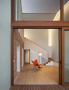Modern minimalist living room with exposed brick walls, wooden flooring, white furniture, and a single orange chair.