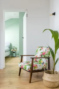 A modern tropical-themed living room featuring a wooden armchair with a floral and bird print cushion, a woven basket with a 