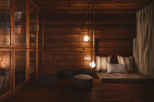 A cozy industrial living room with wooden walls, a wooden bench with pillows, and three round poufs in a dimly lit room.