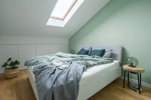 Modern, minimalist bedroom with green walls, a bed with light blue bedding, and a window with a light wood frame.