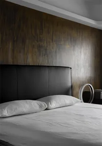Minimalist bedroom featuring a brown leather bed with white bedding, against a textured brown wall