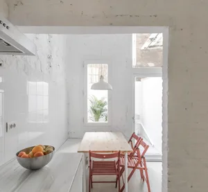 Modern minimalist kitchen with marble countertops and wooden dining table and chairs.
