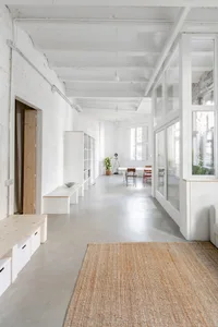 Minimalist workspace with white concrete floors, glass partitions, and simple furniture.