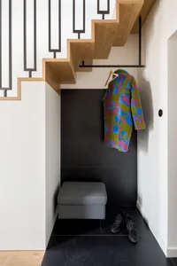 A modern entryway featuring a wooden staircase with a black railing and a colorful coat hanging on a hook.
