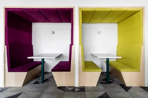 A photograph of two modern cafe booths with purple and yellow upholstered walls and white tables.