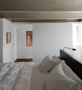 A minimalist bedroom featuring a concrete headboard, white bedding, and a simple, uncluttered space.