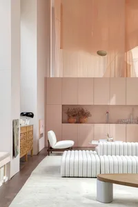A minimalist living room with neutral tones, featuring a white sofa, a wooden coffee table, and a cabinet with open shelves.