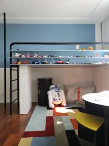 現代兒童房內設有高架床，床邊層架展示玩具，搭配彩色地毯及附有坐墊的休憩區