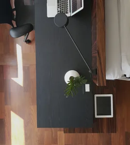 A minimalist workspace featuring a black wooden desk with a laptop, tablet, and lamp.