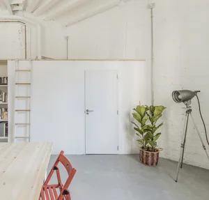 A minimalist living space with concrete walls, a white door, and a red chair.