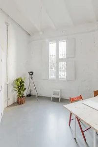 A minimalist office with concrete walls, a white table, and a window with white shutters.