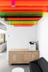 A minimalist office space featuring a wooden desk, a black sofa, and a colorful ceiling design.
