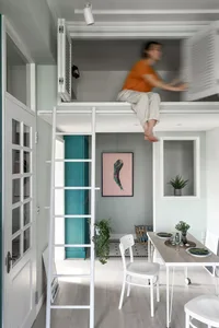 Minimalist design featuring a concrete loft with a white ladder, a dining table, and a person sitting on the loft.