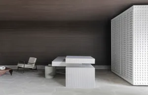 A minimalist office space featuring a concrete desk and chair with a large perforated metal screen.