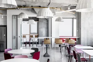 Modern canteen area featuring concrete walls, minimalist lighting, and colorful plastic chairs and tables.