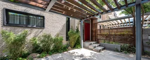 Modern house entryway featuring brick walls, concrete steps, and a wooden pergola.