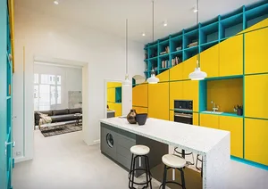 Modern kitchen with yellow and teal cabinets, white countertops, and pendant lights.