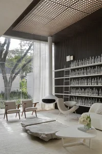 A minimalist living room with glass walls, a white coffee table with a flower arrangement, and a bookshelf filled with clear