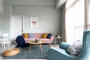 Scandinavian living room featuring a blue and pink couch with cushions, a wooden coffee table, a round stool, framed deer art