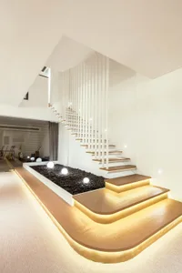A minimalist living room with a wooden staircase featuring embedded lighting and a black rock garden.