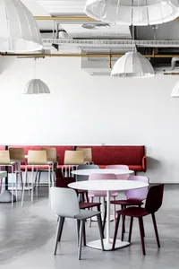 A modern restaurant interior with white tables, colorful chairs, and a red bench seating area.