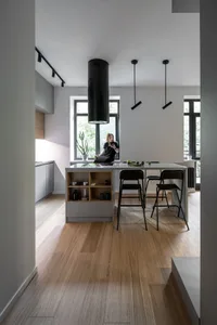 Modern kitchen interior featuring a kitchen island with a light wood floor, black stools, and a black hood.
