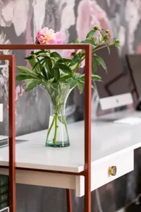 Close-up of a modern home office with a glass vase containing pink flowers, placed on a desk.