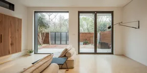 A modern living room with concrete floors and wood paneled walls, featuring a comfortable seating area and large windows for 