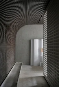 A minimalist concrete lobby interior with ribbed metallic panels and a textured marble floor.