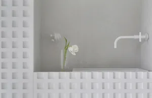A minimalist modern bathroom with concrete walls, a white bathtub, and a white vase with a white flower on the edge of the tu
