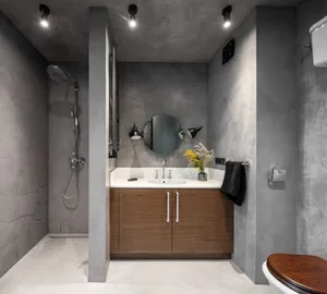 A modern bathroom with concrete walls, a wooden vanity, and industrial-style lighting.