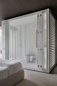 A modern bathroom with a white plaster shower enclosure and a white bed in the foreground.