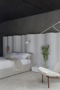 Modern minimalist bedroom with concrete walls, white furniture, and a single potted plant on a side table.