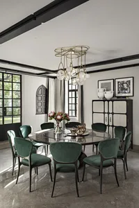 A modern dining room featuring a round table with marble top, surrounded by green velvet chairs with black frames, and a hang