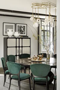 Modern dining room featuring a marble table, green velvet chairs, and elegant chandelier.